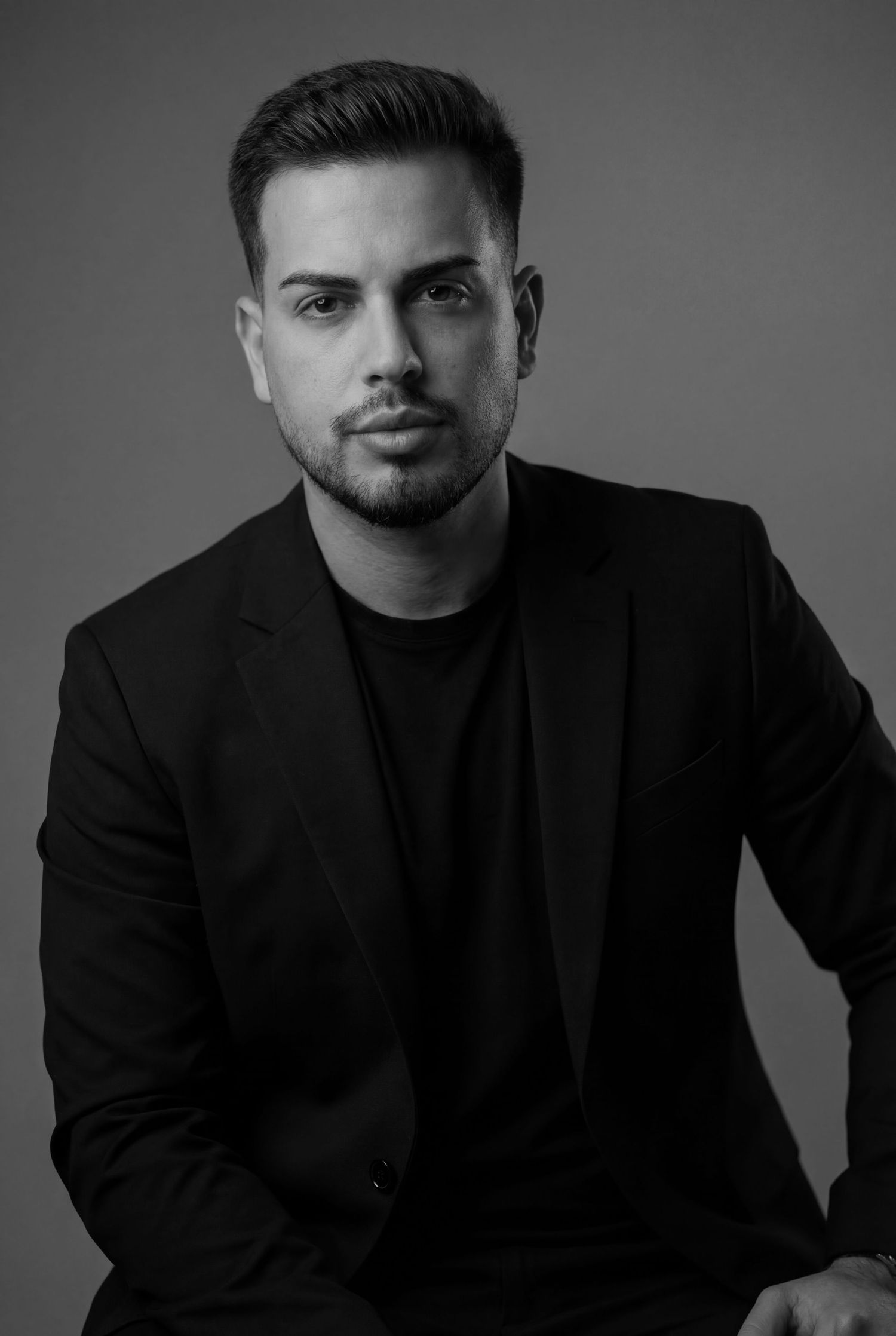 Black and white portrait series showing a person in dark attire against a simple background in dramatic lighting.