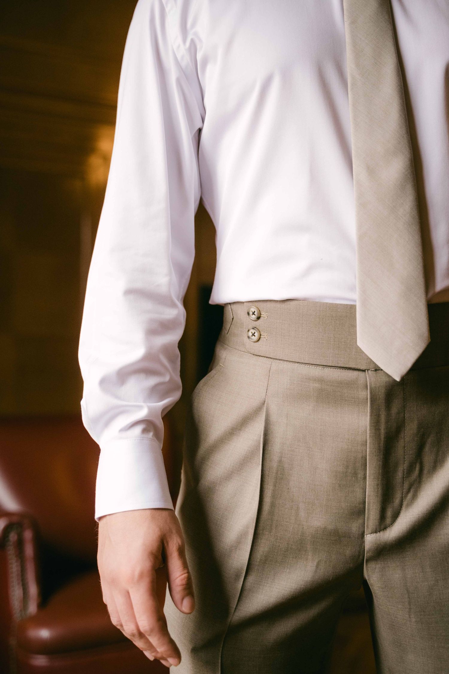 Close-up view of formal attire showing a crisp white dress shirt, light gray tie and high-waisted tan dress pants.