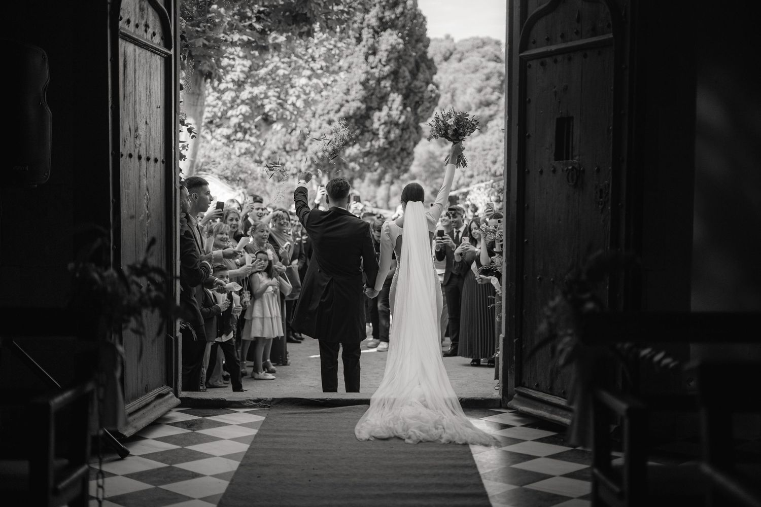 Black and white photo showing a wedding celebration inside a grand church doorway with guests lining the aisle.