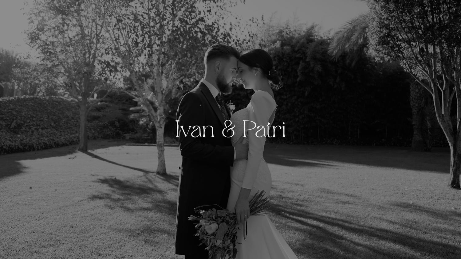 A romantic black and white wedding photo showing a couple embracing outdoors on a sunny day with trees in the background.