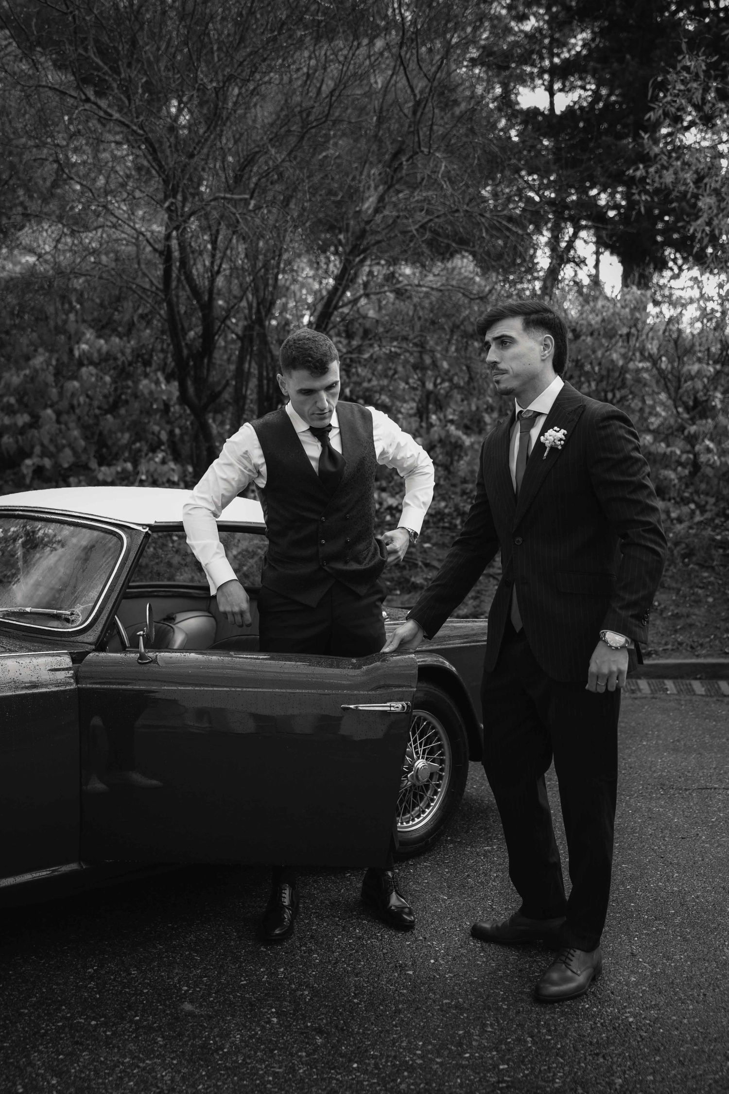 Black and white photo series showing men in formal attire examining and leaning on a classic car at an outdoor event.