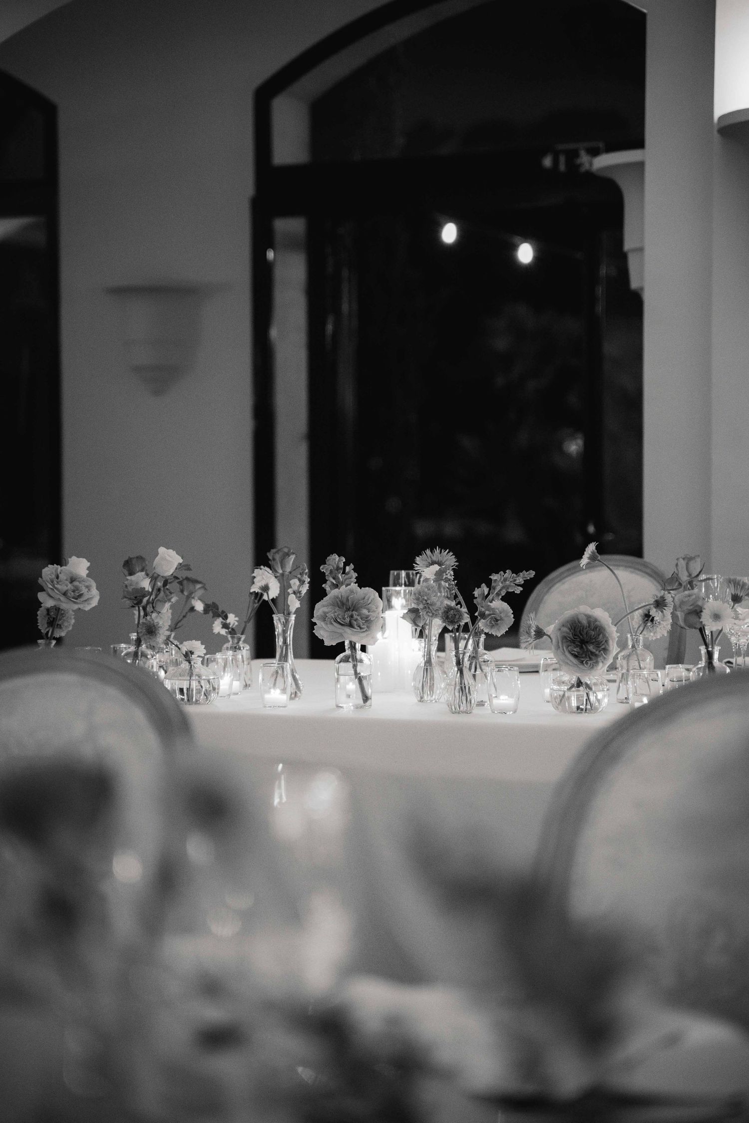 Elegant table settings with crystal glassware arranged on white tablecloths in a dimly lit reception hall.