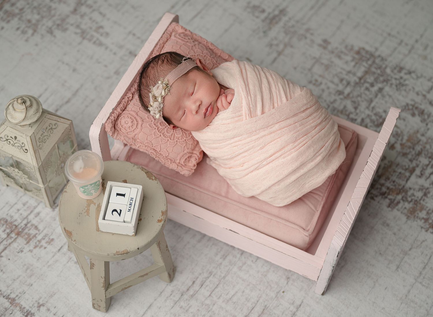 Newborn baby sleeping peacefully on pink miniature bed with vintage decor and soft lighting.