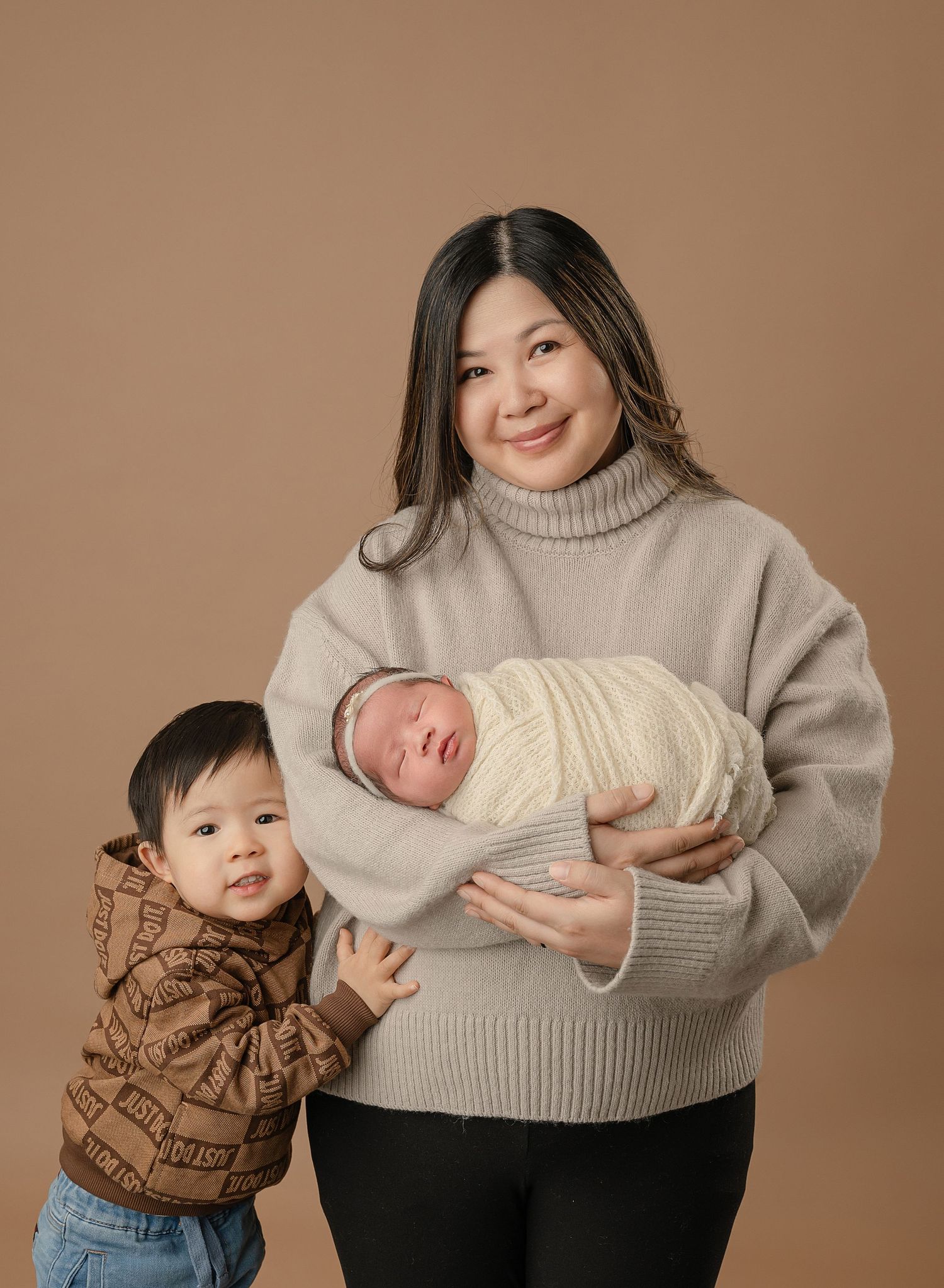 A heartwarming family moment with a toddler and newborn baby with their parent in cozy winter sweaters.