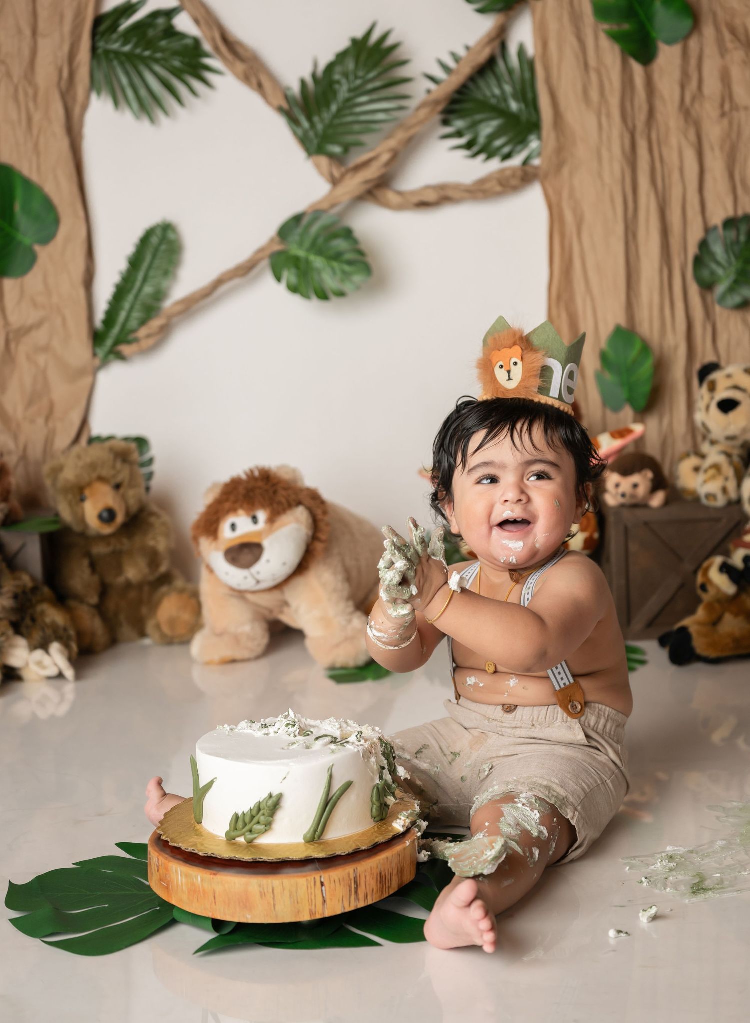 A cake smash photo session featuring a rustic woodland theme with stuffed animals and tropical leaves as decorations.