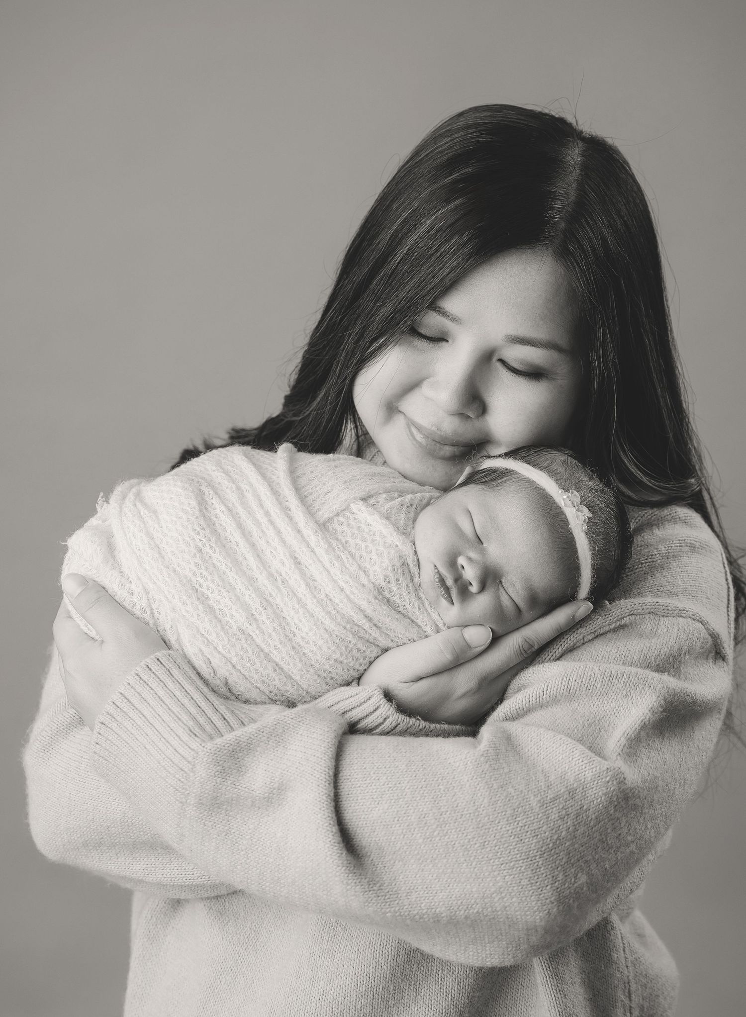 Black and white portrait of a parent tenderly holding a swaddled sleeping newborn.