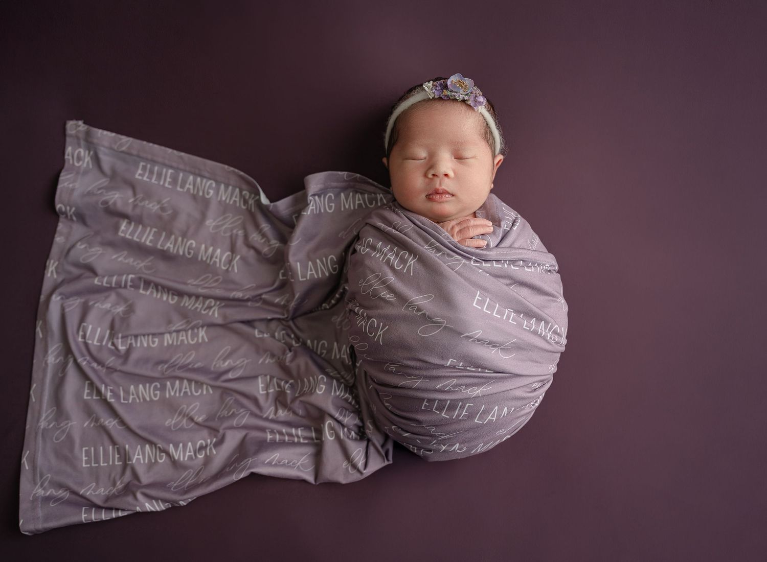 Newborn baby peacefully sleeping while wrapped in gray swaddle blanket on dark background.