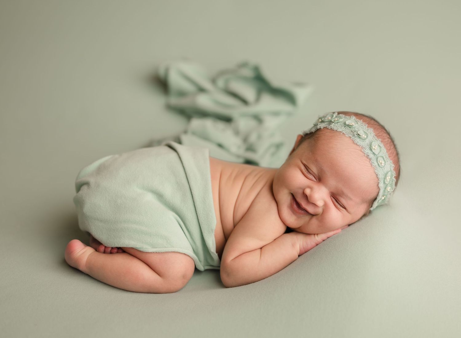 Newborn baby wearing mint green wrap sleeps peacefully during professional photo session.