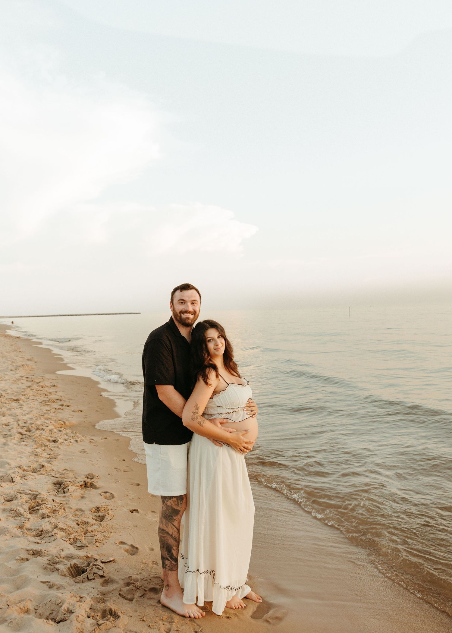 A couple shares a tender moment on the beach with waves rolling in at sunset.