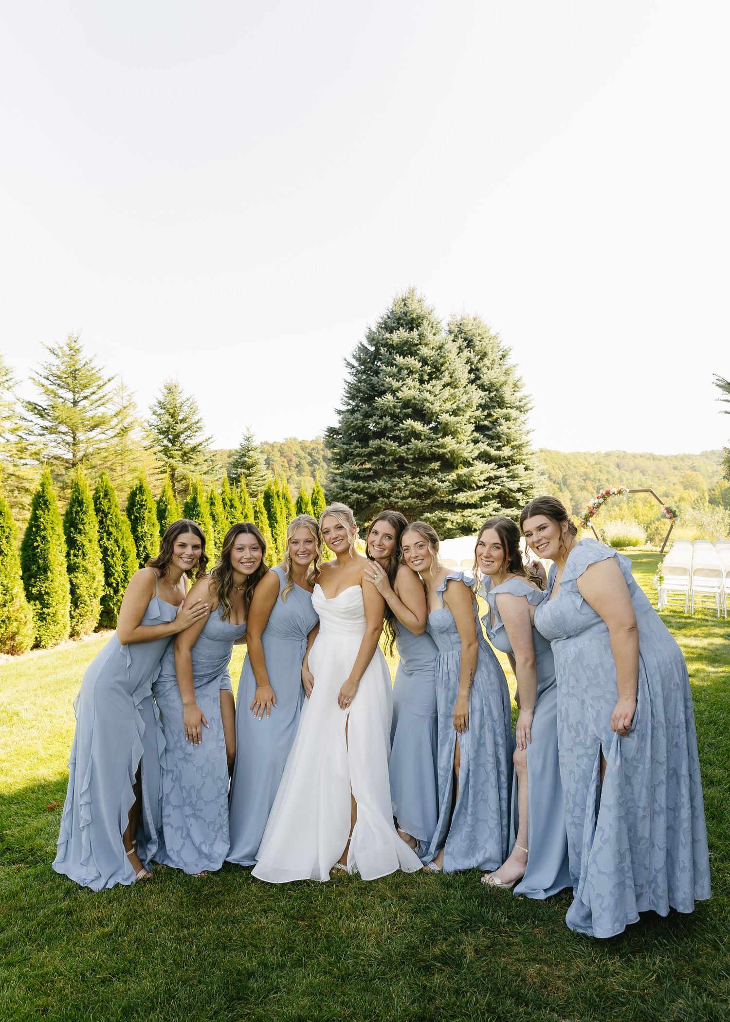 Wedding party in light blue bridesmaid dresses poses together on grassy hillside.