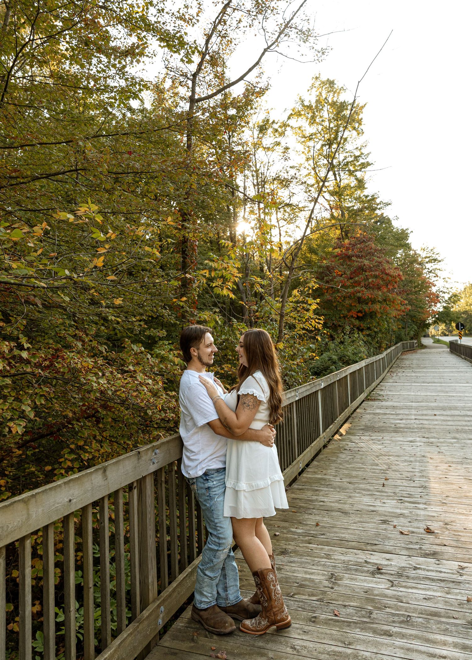 Romantic couple embraces on wooden boardwalk surrounded by autumn foliage.