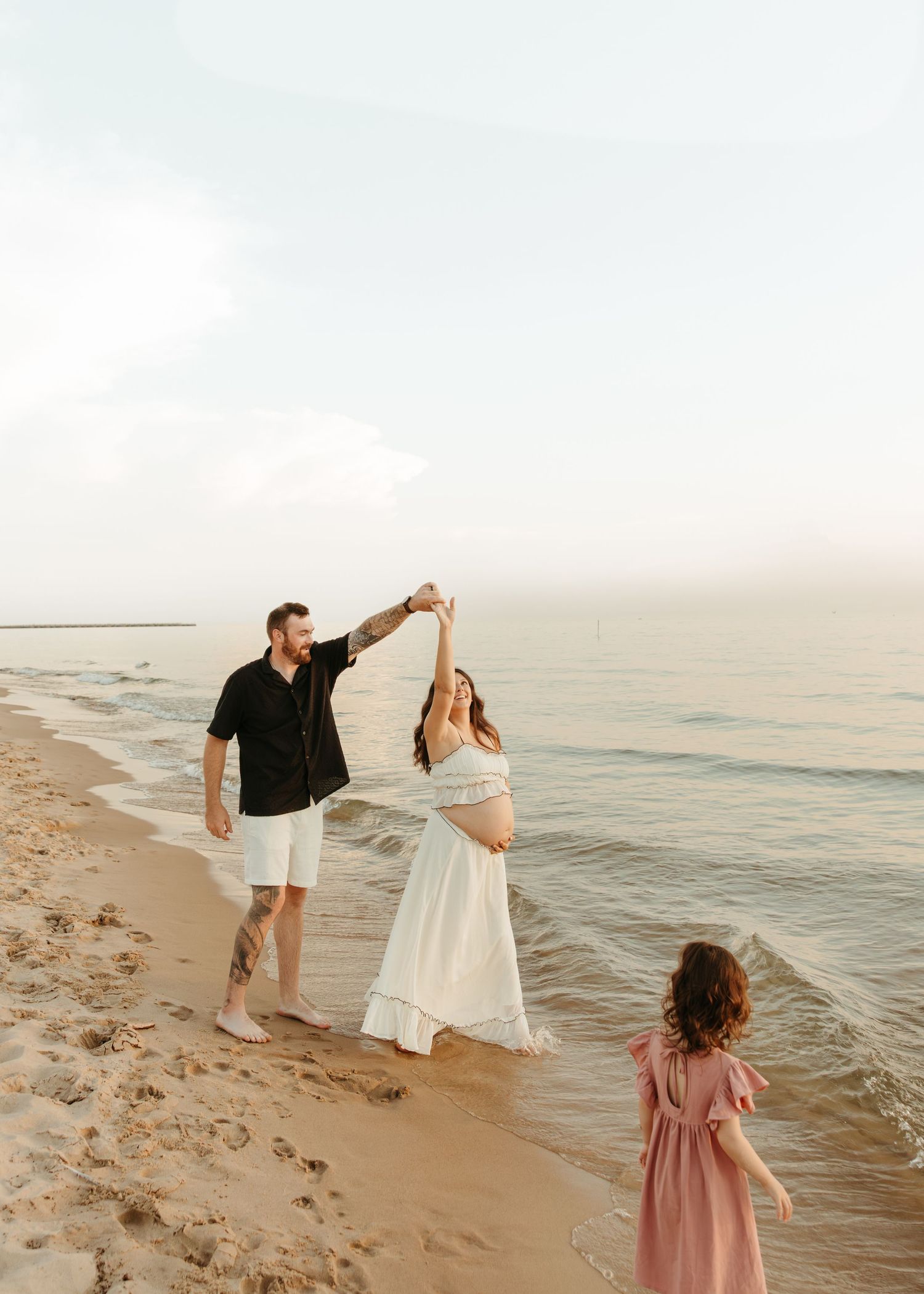 Family enjoying a playful moment dancing together on a sandy beach at dusk.