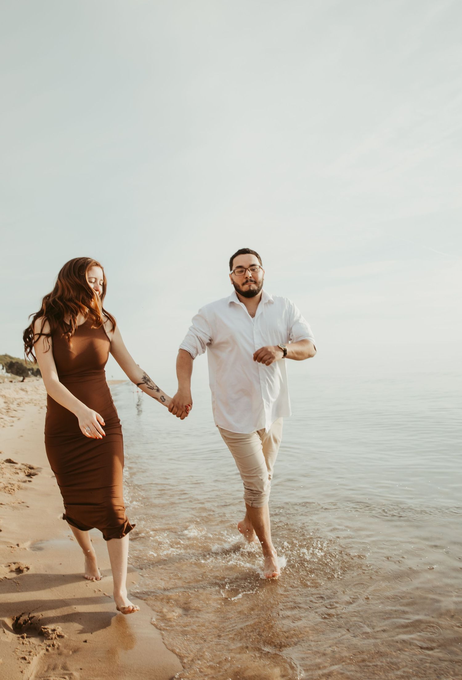 Couple splashing in ocean waves during beach maternity photoshoot.