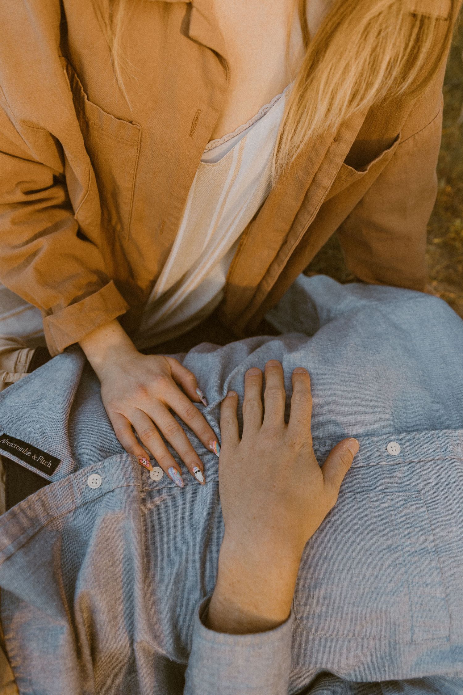 Close-up view of hands unbuttoning a light blue linen shirt.
