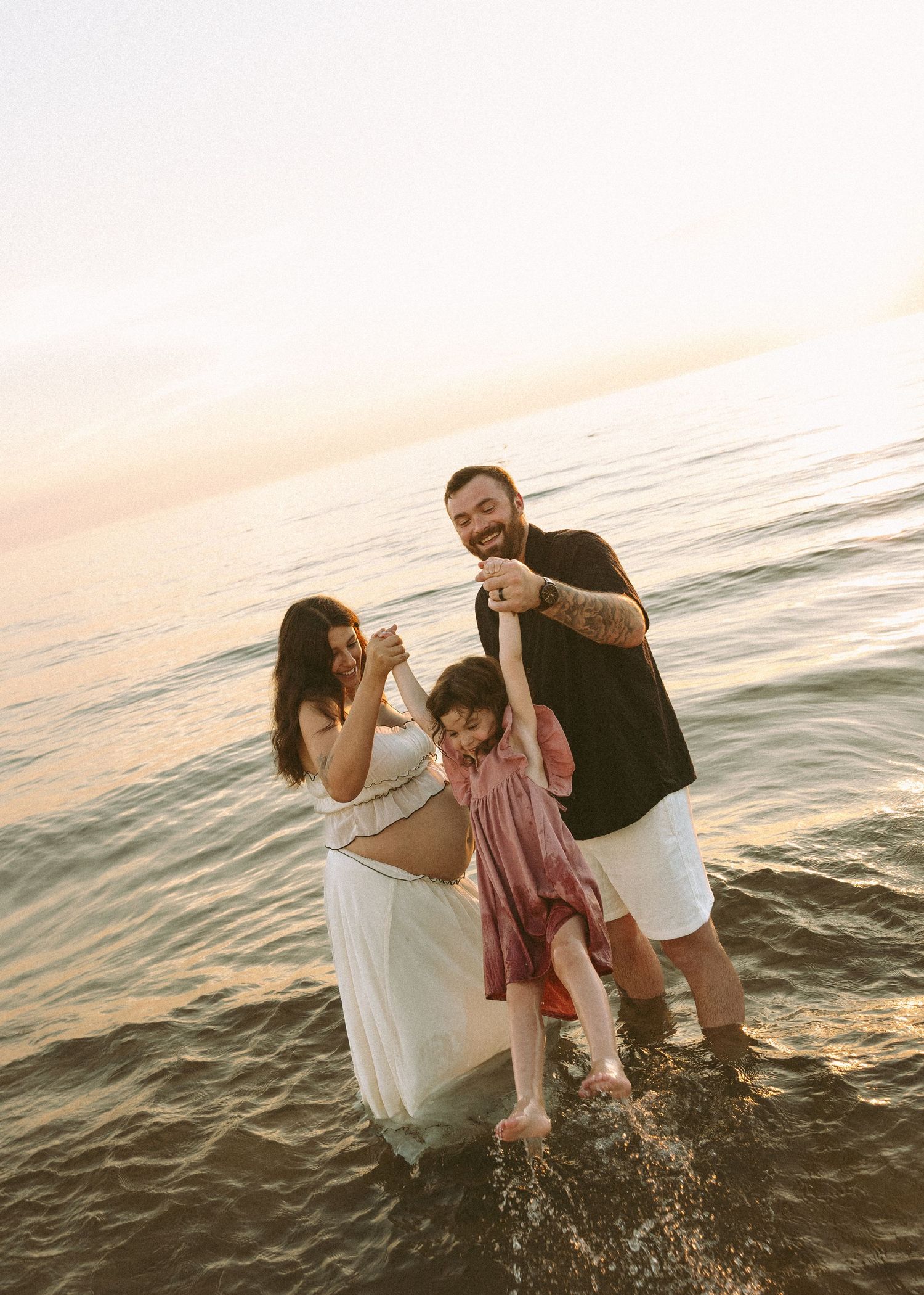 Family playing and splashing in the ocean waves during a sunset beach photoshoot.