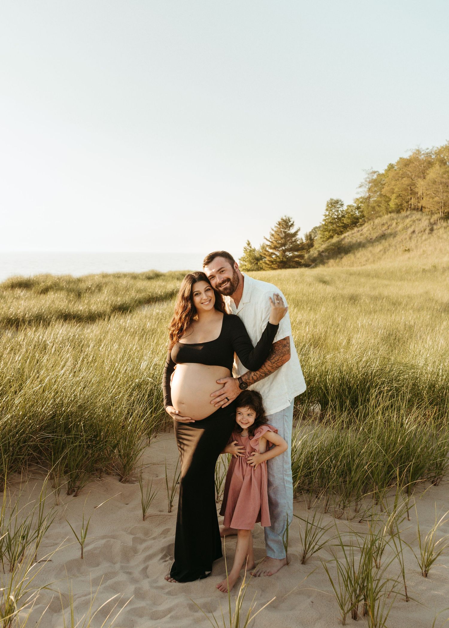 A family poses together on sandy dunes with tall grass at sunset.