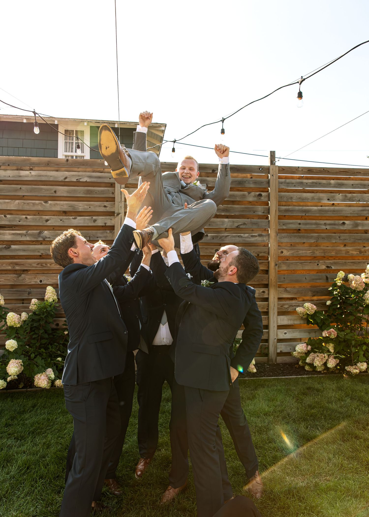 Groomsmen lift and celebrate during outdoor wedding festivities.