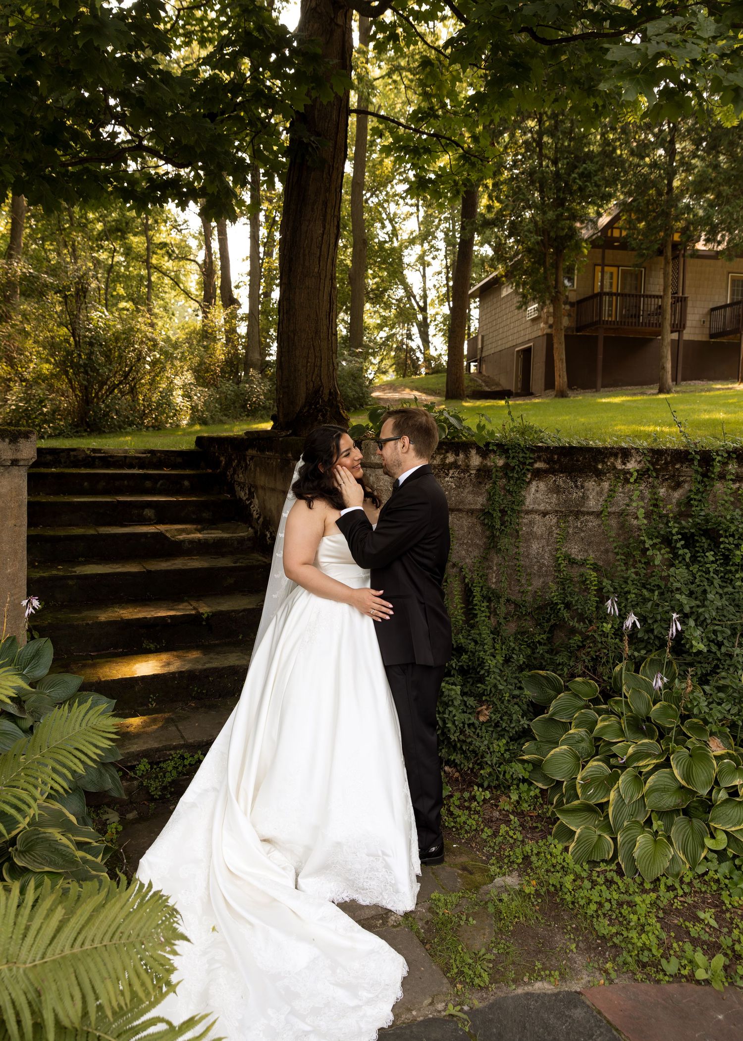 Wedding couple shares intimate moments in a garden setting with stone steps and greenery.