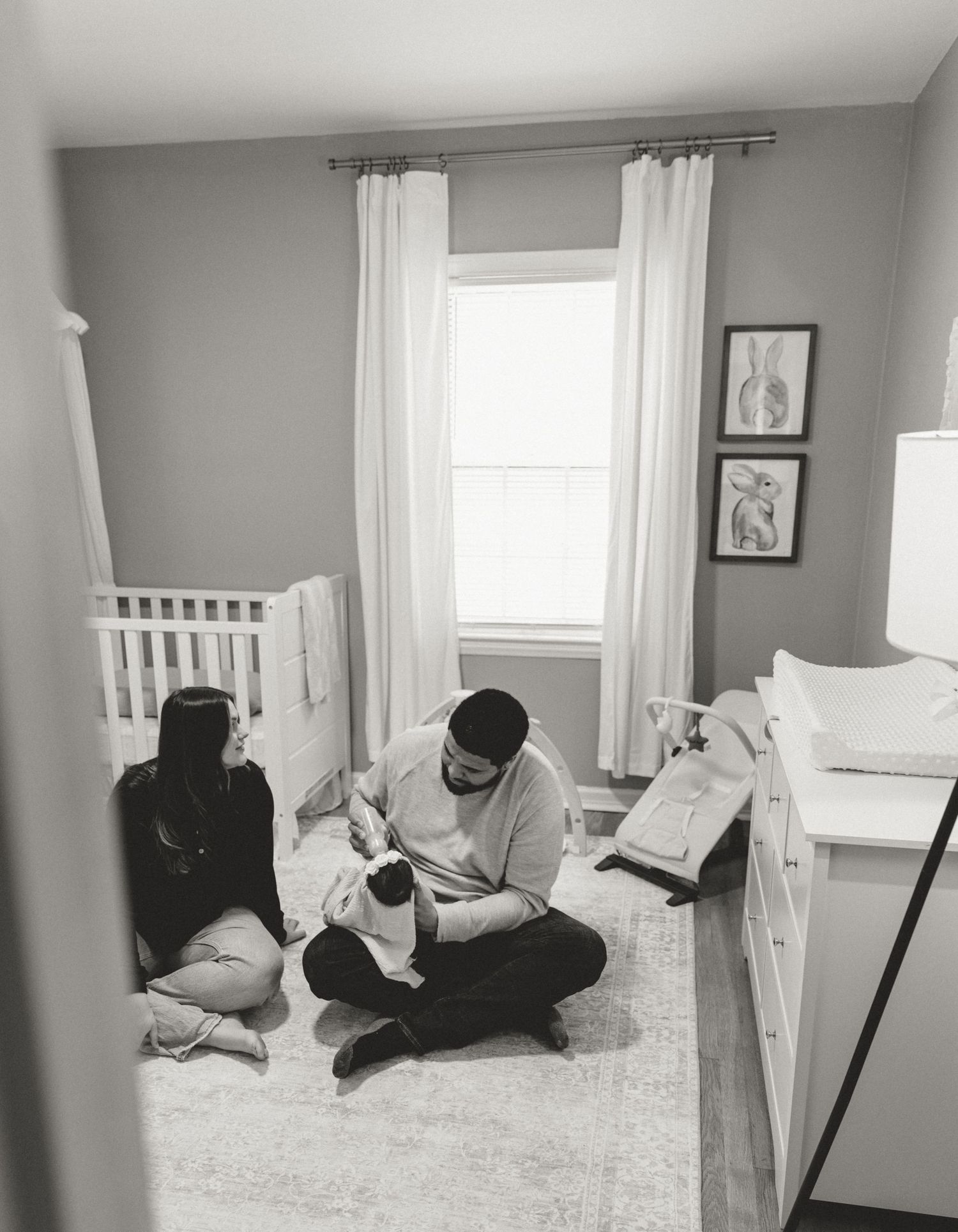 Black and white photo of a family playing together on a carpeted floor in a bright room.