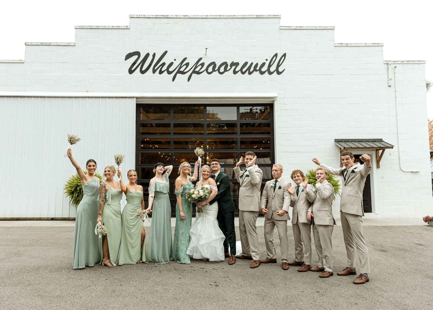 Wedding party celebrating outside Whippoorwill venue, bridesmaids in mint gowns and groomsmen in tan suits cheering.