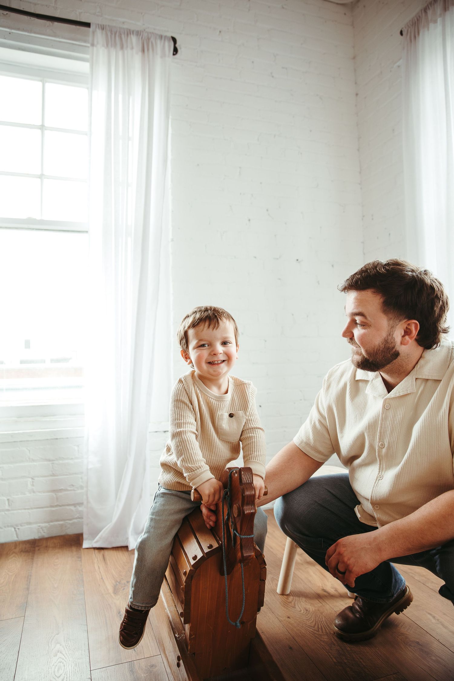 Father and child playing with wooden rocking toy in bright room.