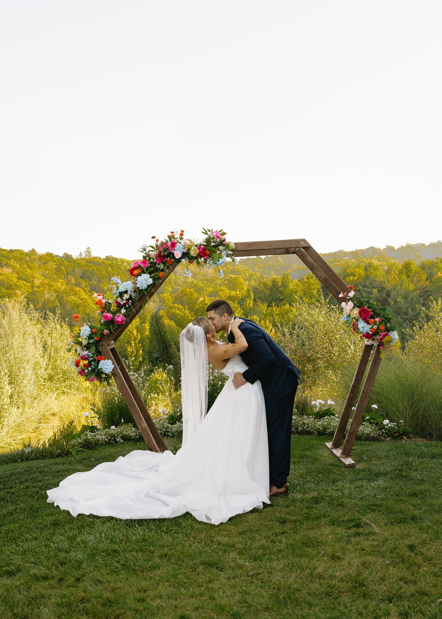 Wedding ceremony setup with wooden arch decorated with flowers against rolling hills.