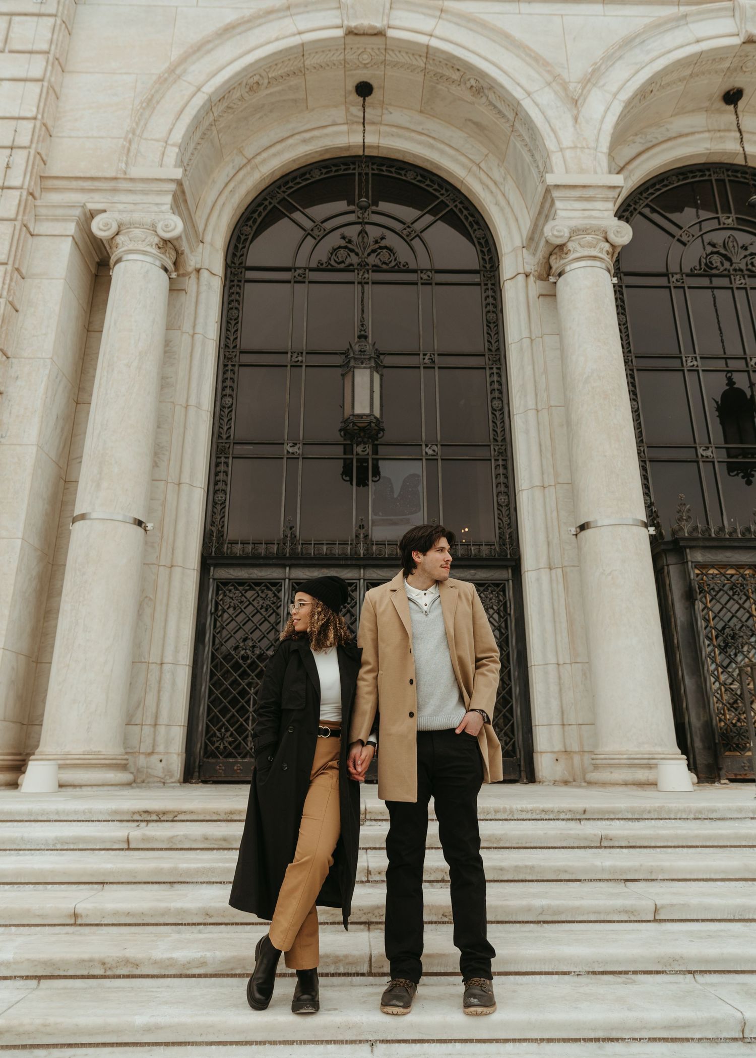 Two people pose casually on white stone steps with ornate archways behind them.