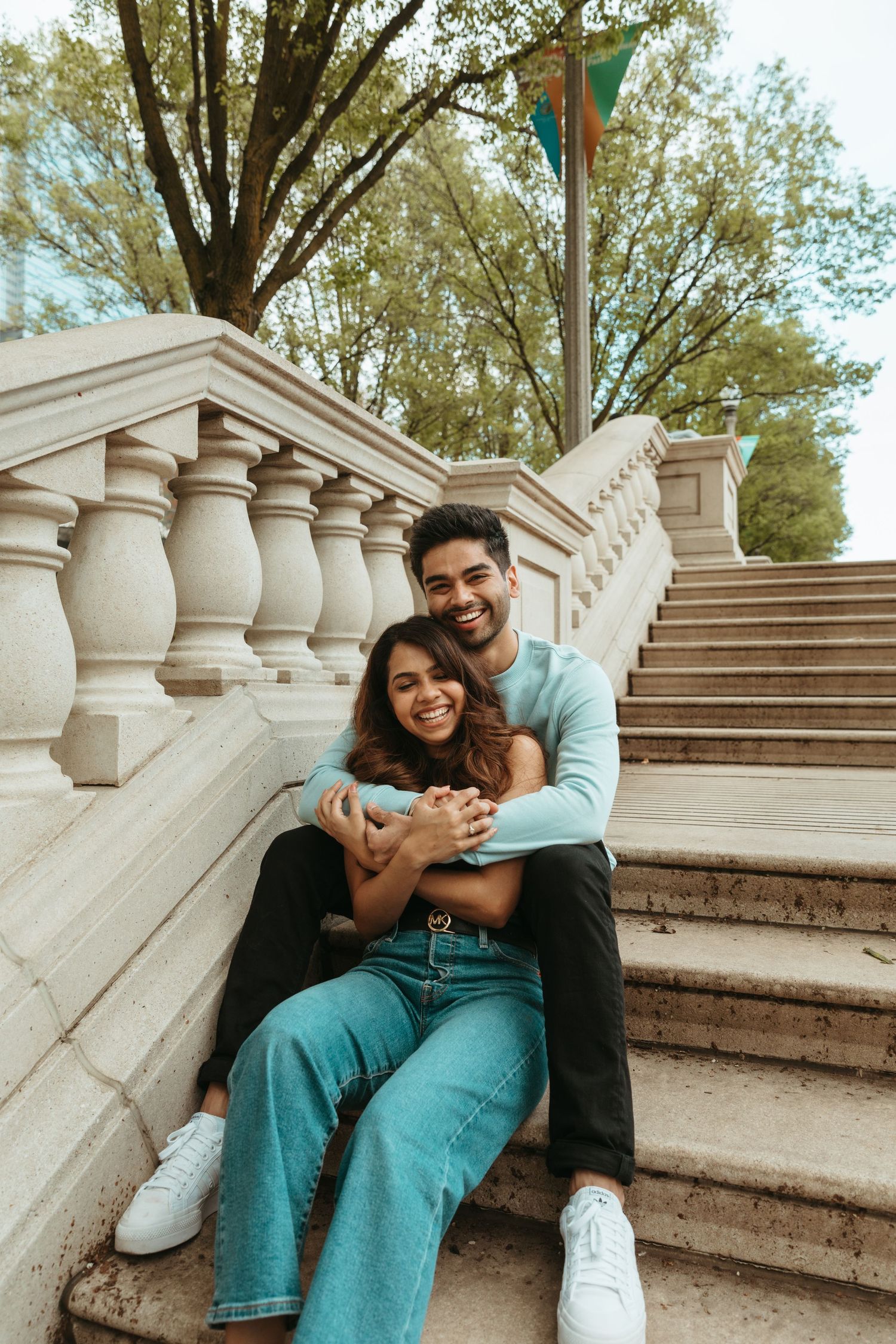 Playful couple shares laughter while posing on stone steps with decorative balusters in an outdoor setting.