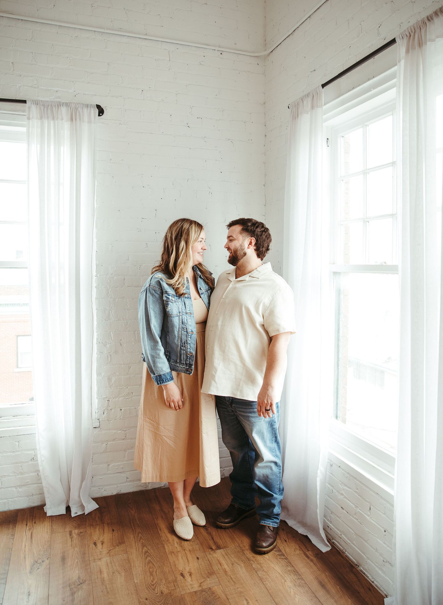 Family posing in minimalist white room with large windows.