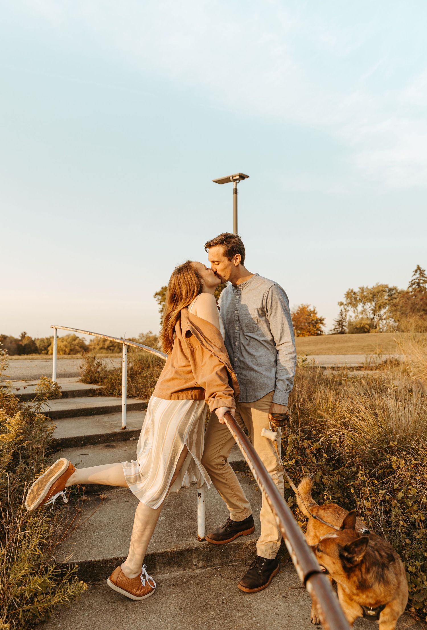 Romantic couple sharing a moment on a pathway with their dog during sunset.