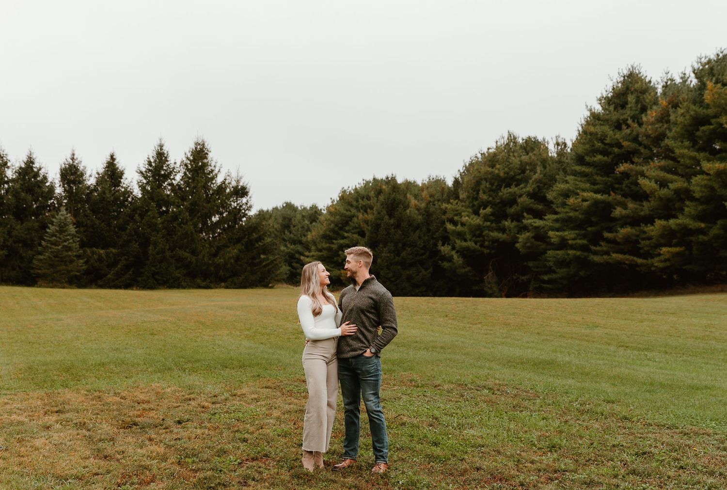 A couple laughs together while taking photos in a scenic meadow.