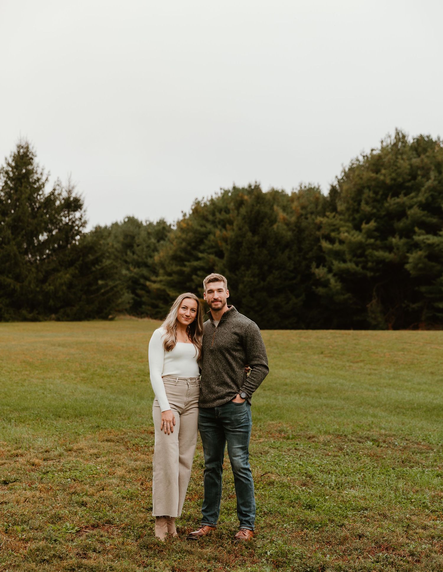 A couple shares a candid moment while standing in a grassy field on an autumn day.