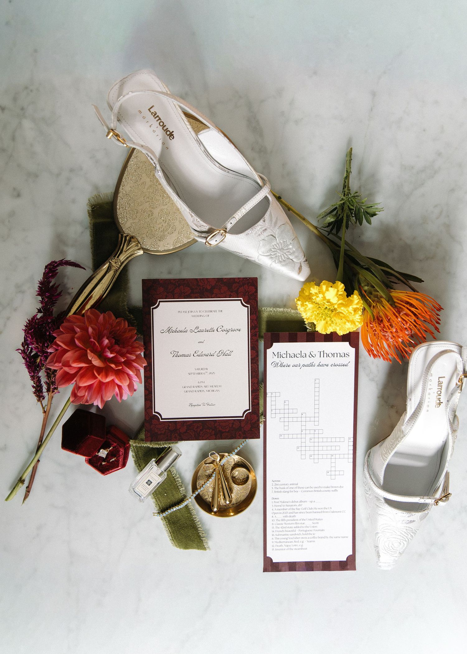Wedding invitation suite with burgundy details and floral elements arranged on marble surface.
