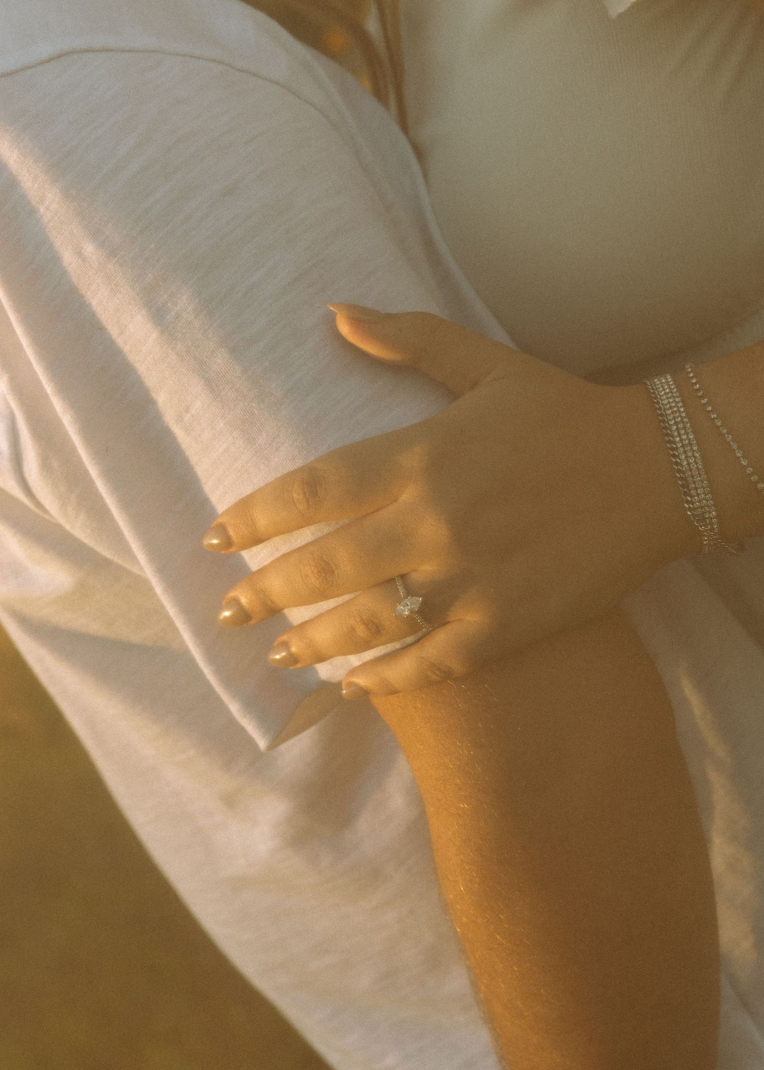 Close-up of a hand wearing an engagement ring against a soft golden background.