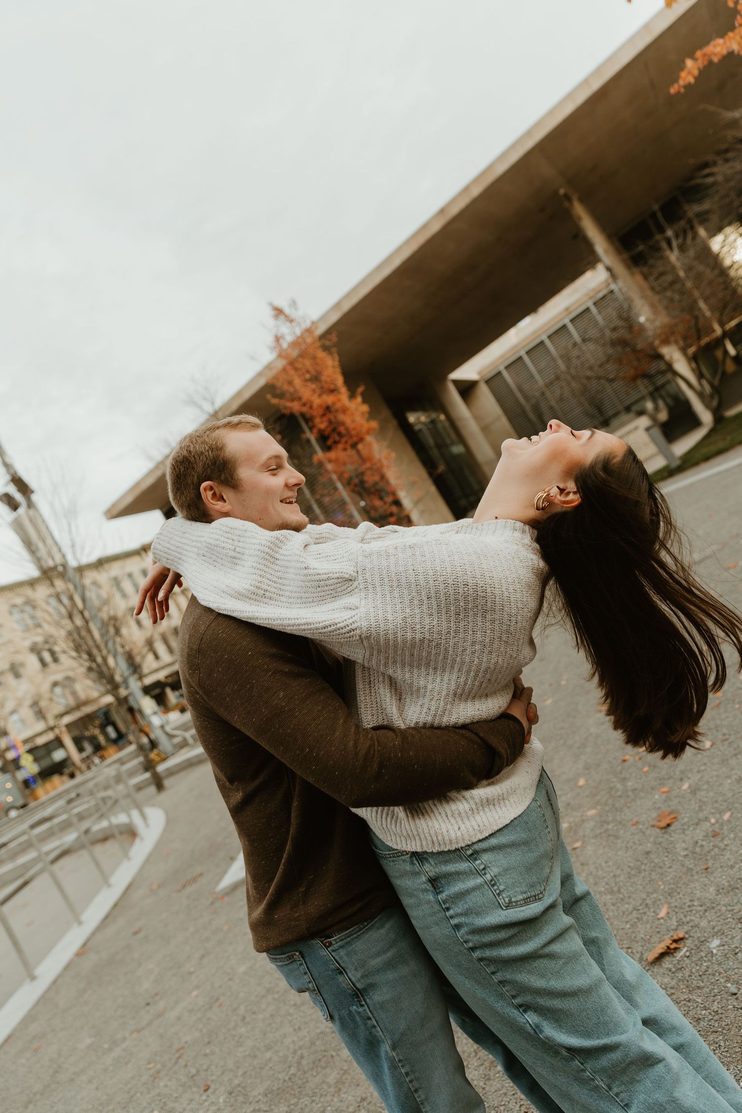 Playful couple spinning and dancing together on autumn street with falling leaves.