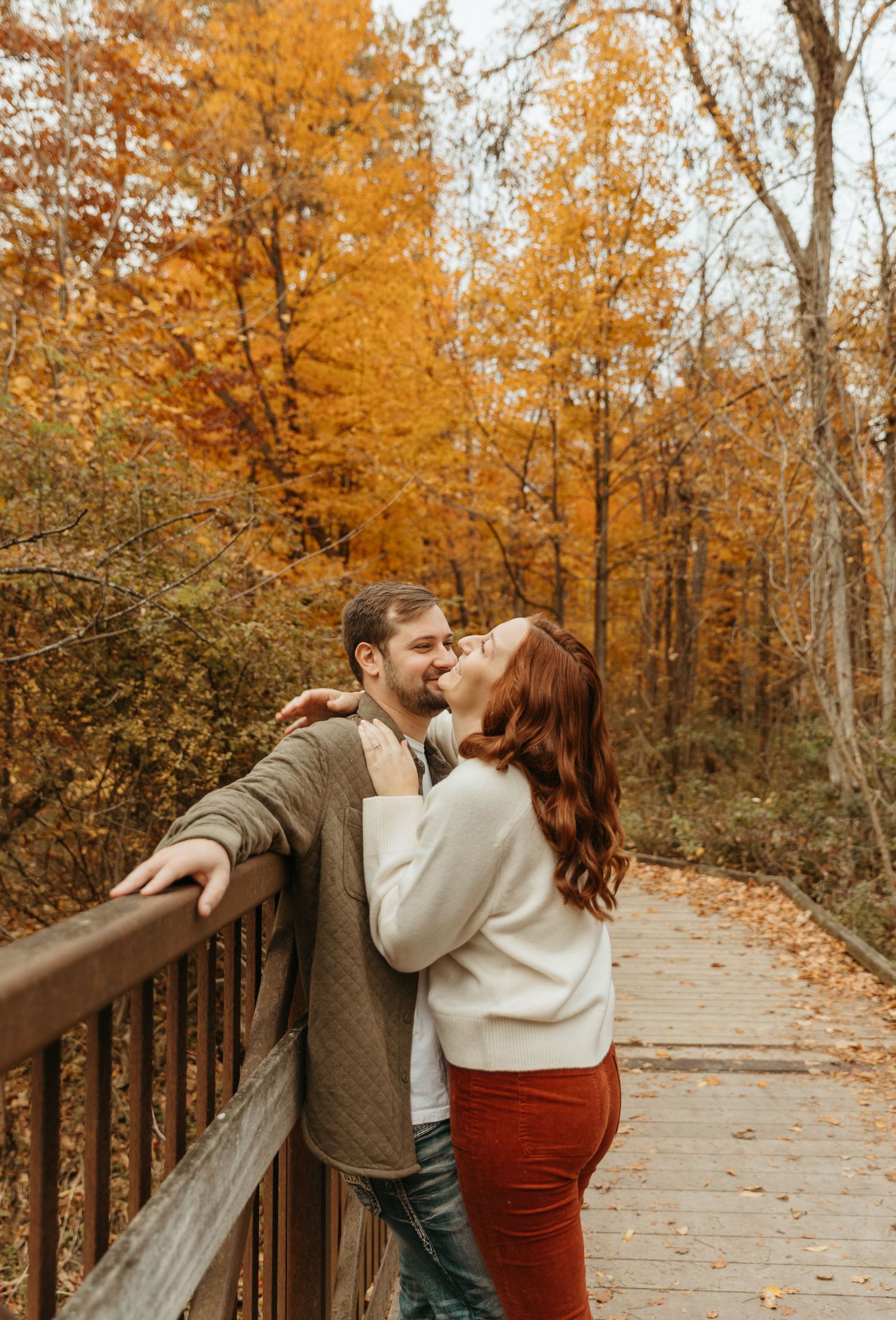 A couple shares a romantic moment on a wooden bridge surrounded by vibrant autumn foliage.