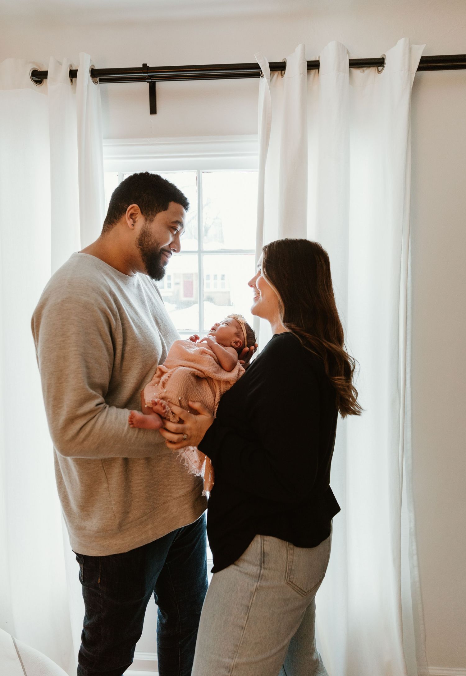 Intimate lifestyle series of parents sharing loving moments with their newborn in a sunlit room.