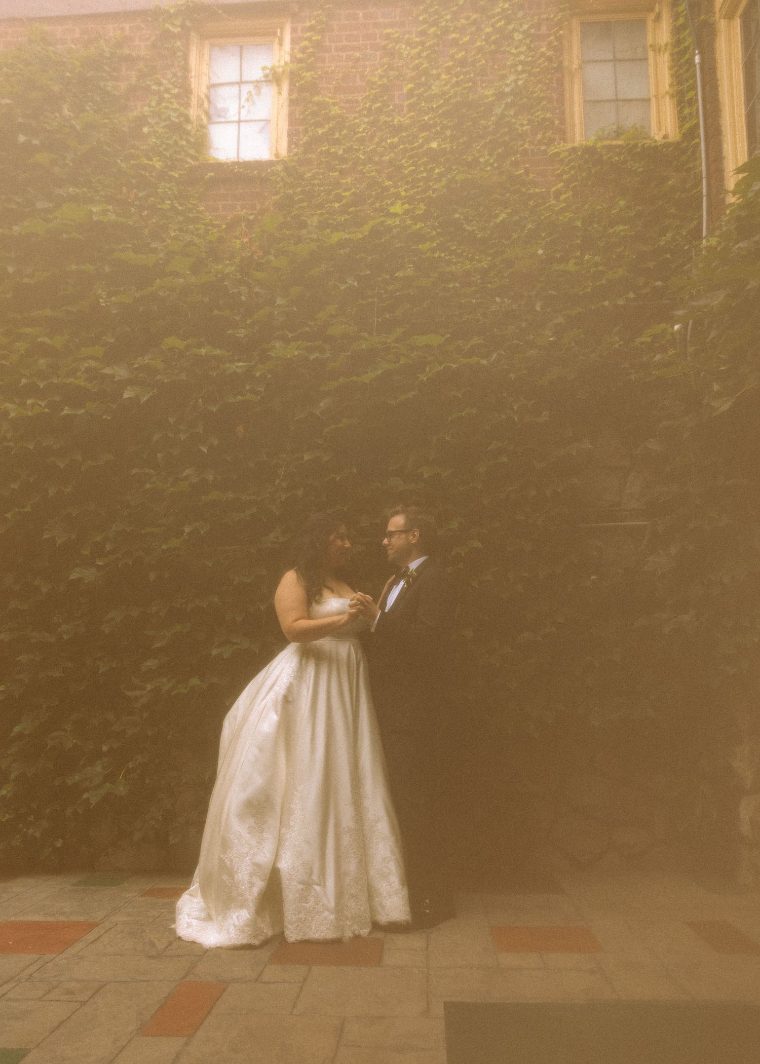 A romantic wedding portrait against a sunlit ivy-covered wall.