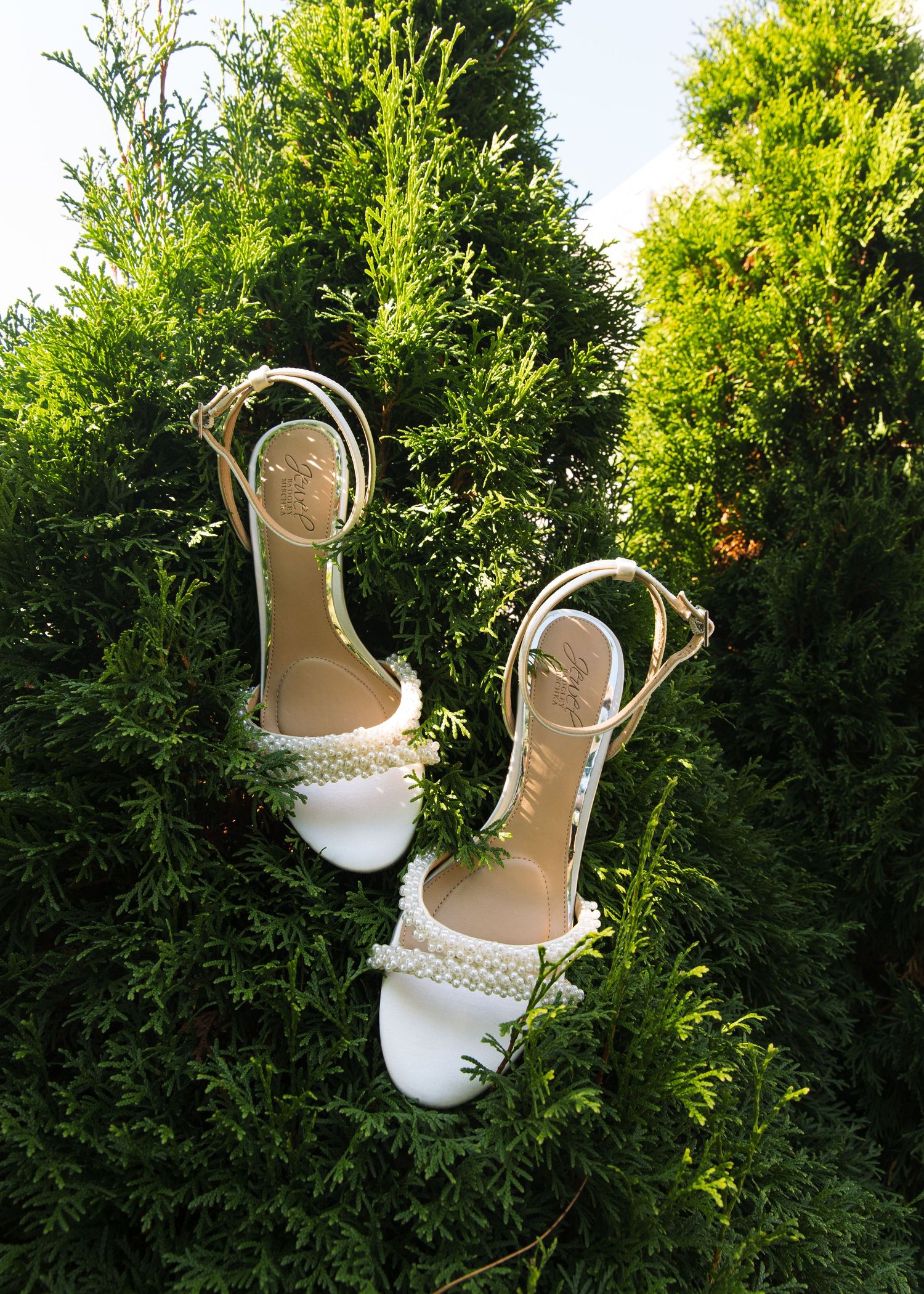 White bridal shoes displayed against green foliage in natural lighting.