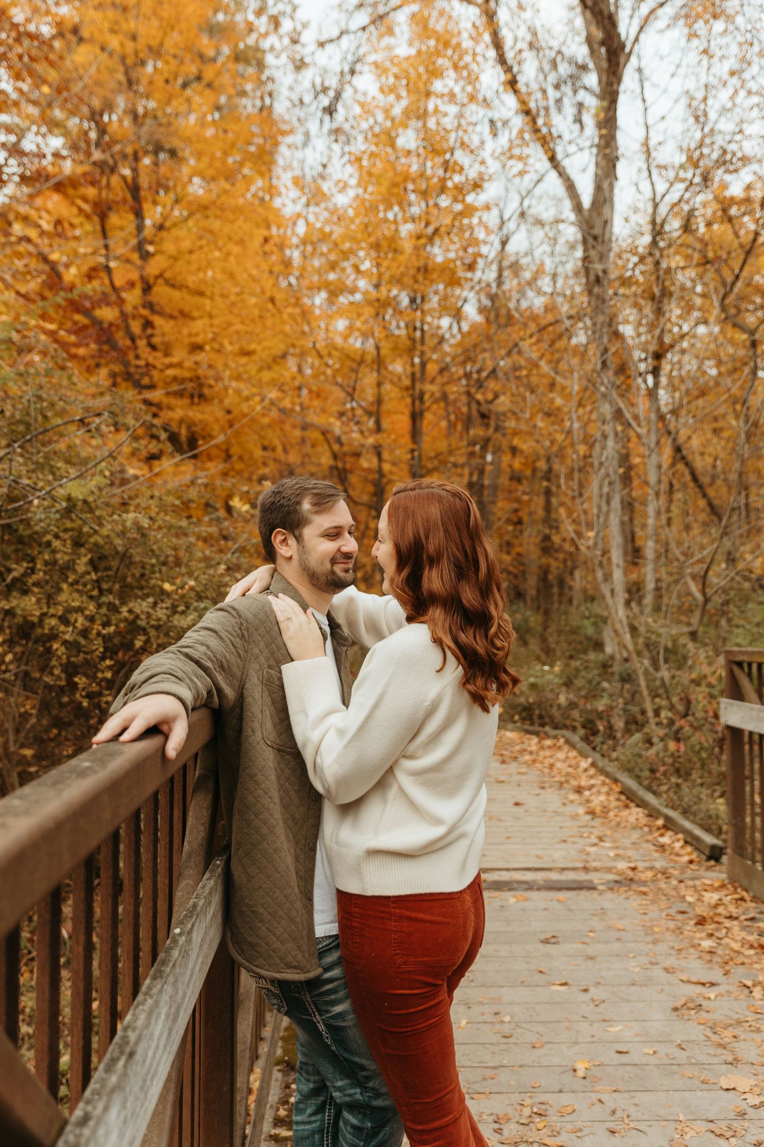 Two people embrace on a wooden walkway surrounded by golden fall trees.