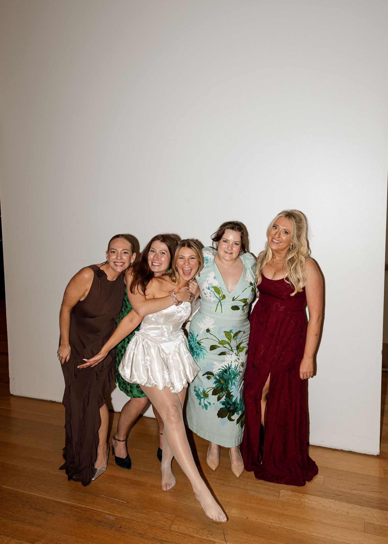 Wedding party members strike fun poses together in a bright indoor space.