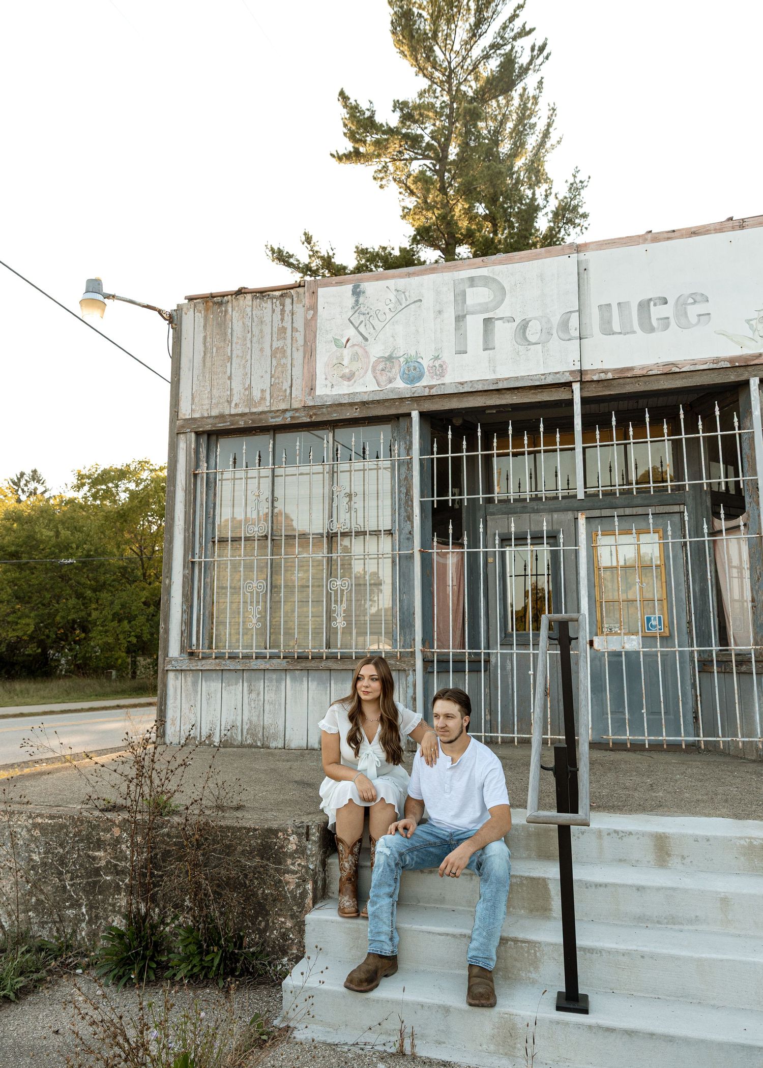 Couple sits on concrete steps outside vintage produce store at sunset.