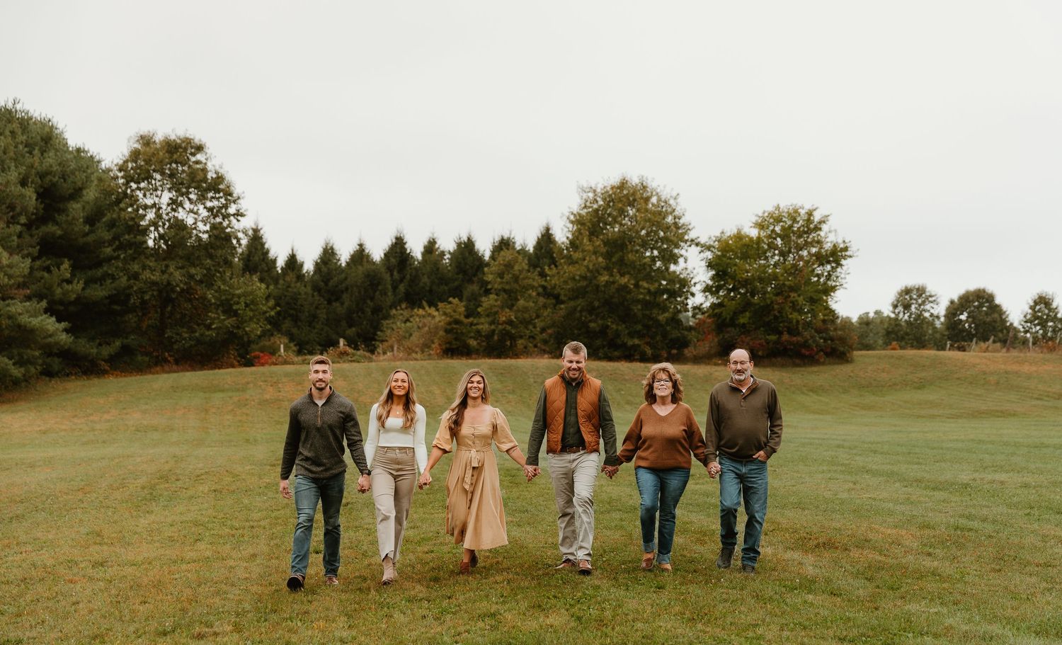 Panoramic shot of people lined up on a rolling green hill during fall season.