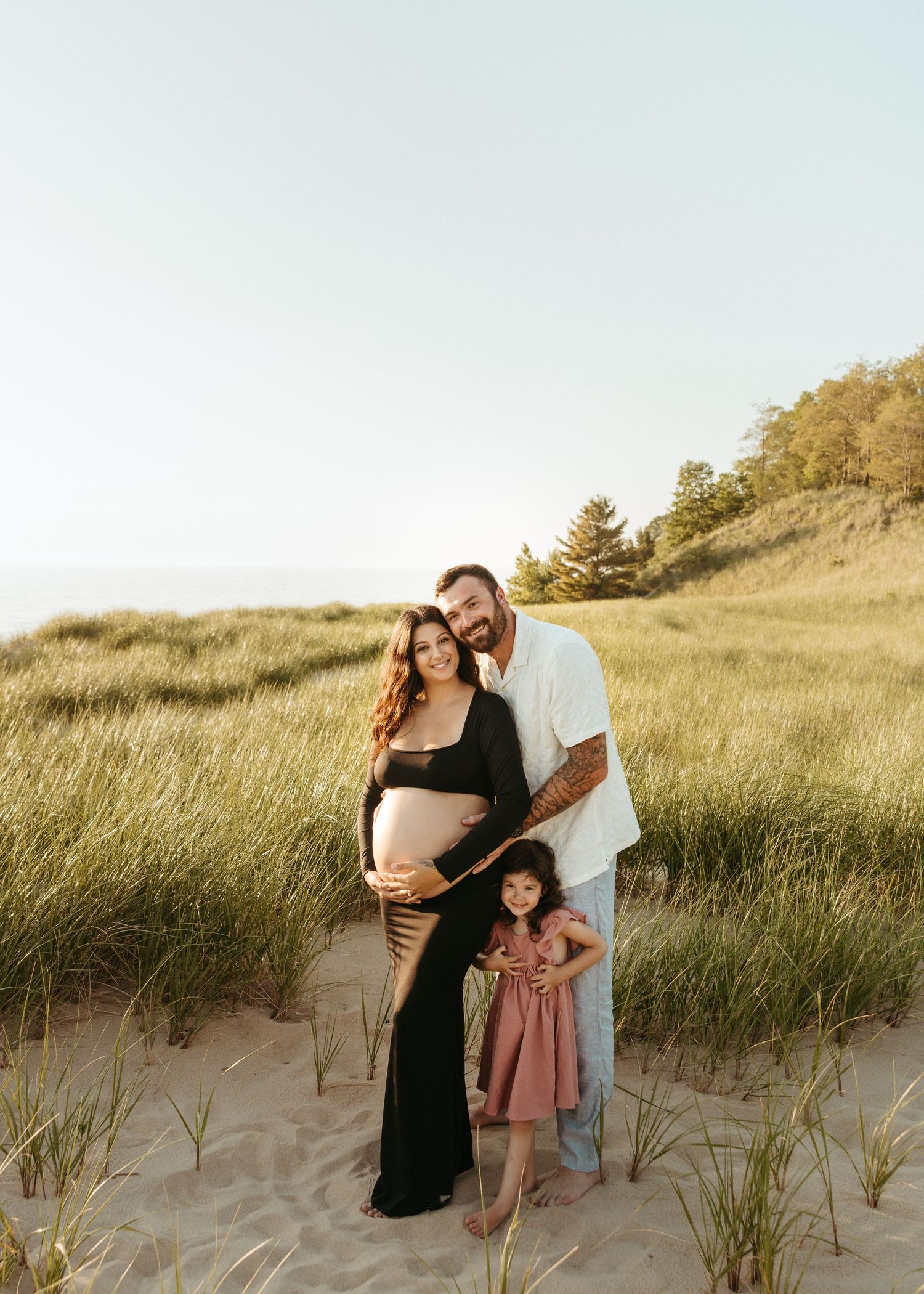 A loving family moment captured among beach grass and sand dunes at golden hour.