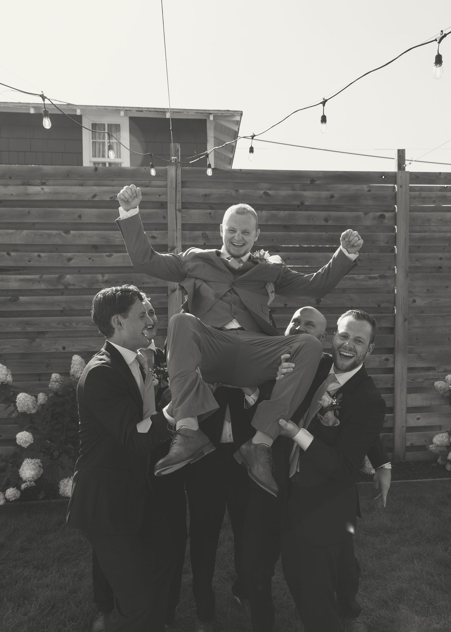 Black and white photo of groomsmen lifting and celebrating outdoors.