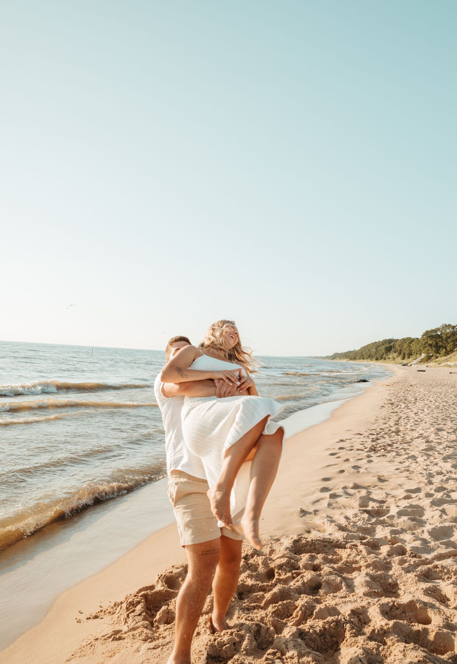 Couple in white clothing dancing together on beach during sunset.