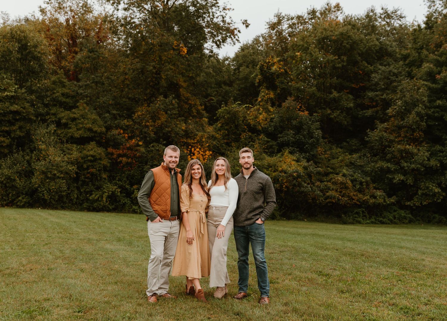Family portrait composition on a hillside with fall foliage in the background.