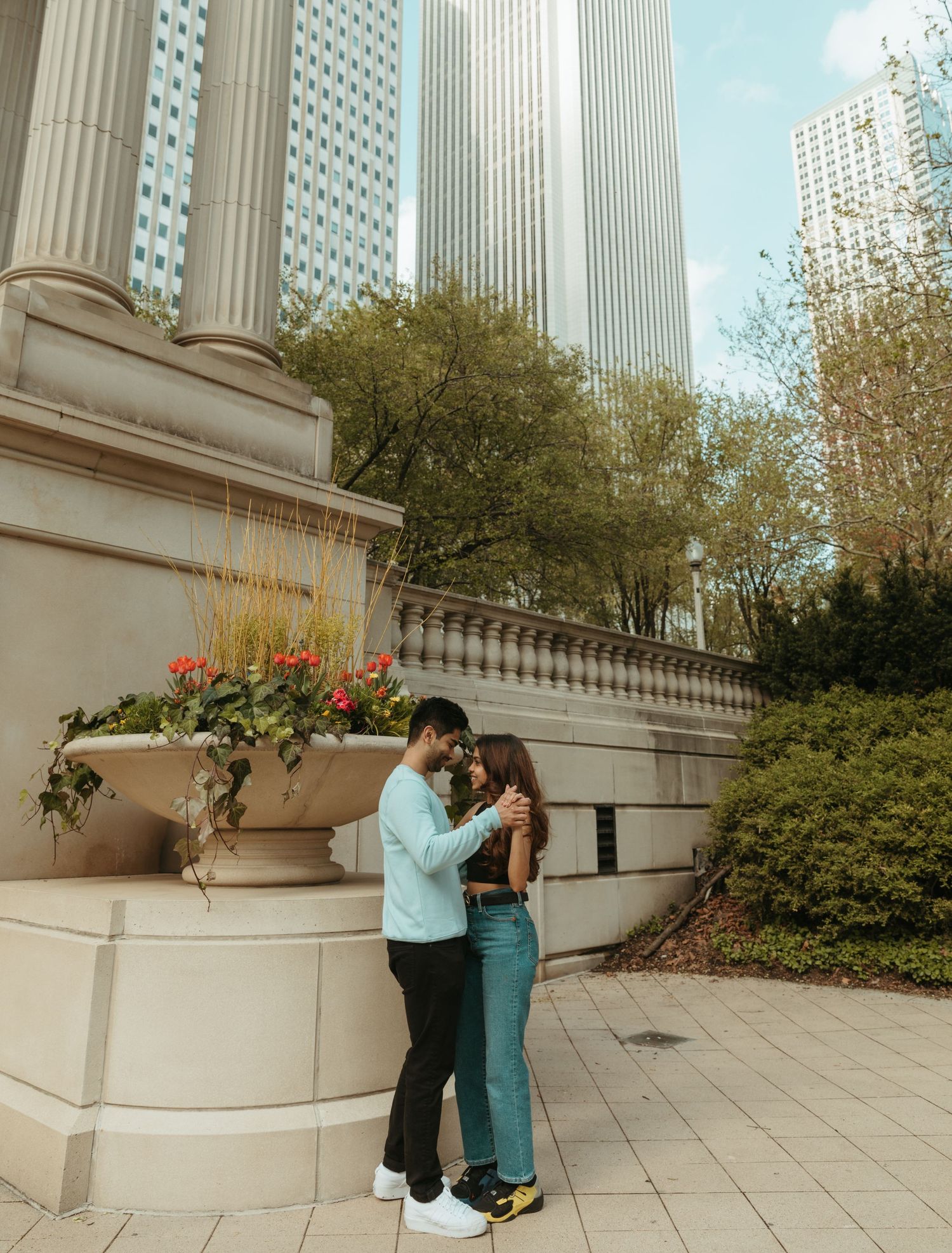 Romantic couple interacting near white stone wall with columns and planters in urban setting.