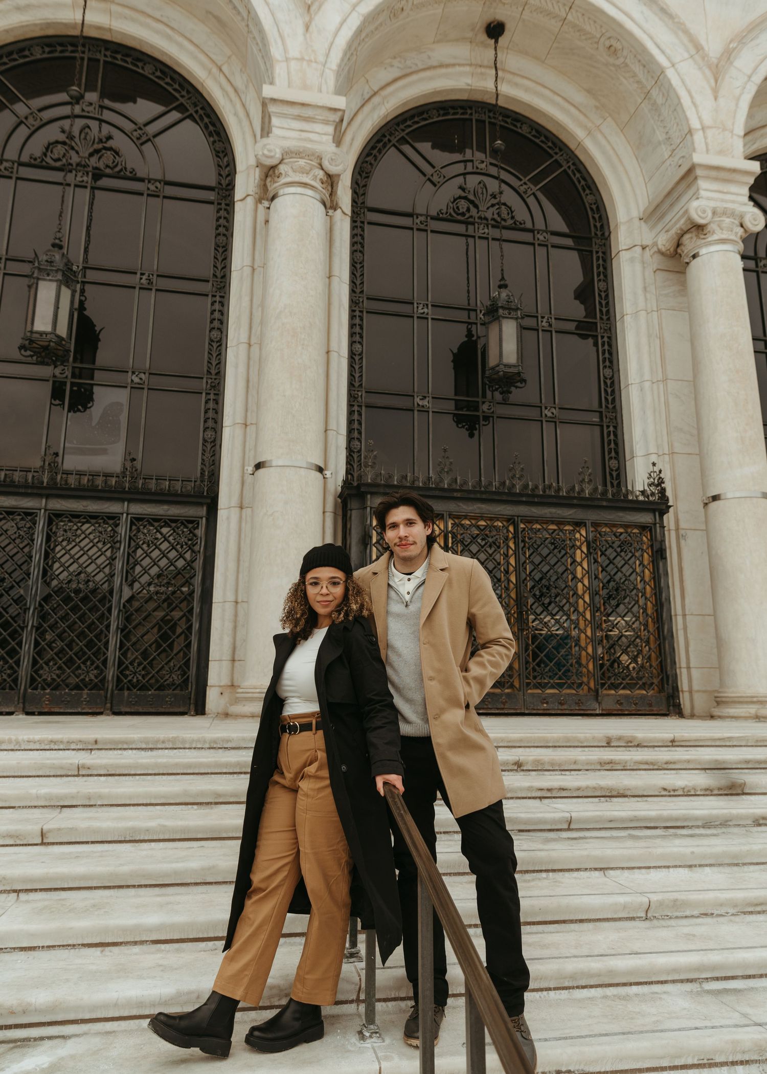 Two people sit and pose playfully on white marble steps of a historic building.