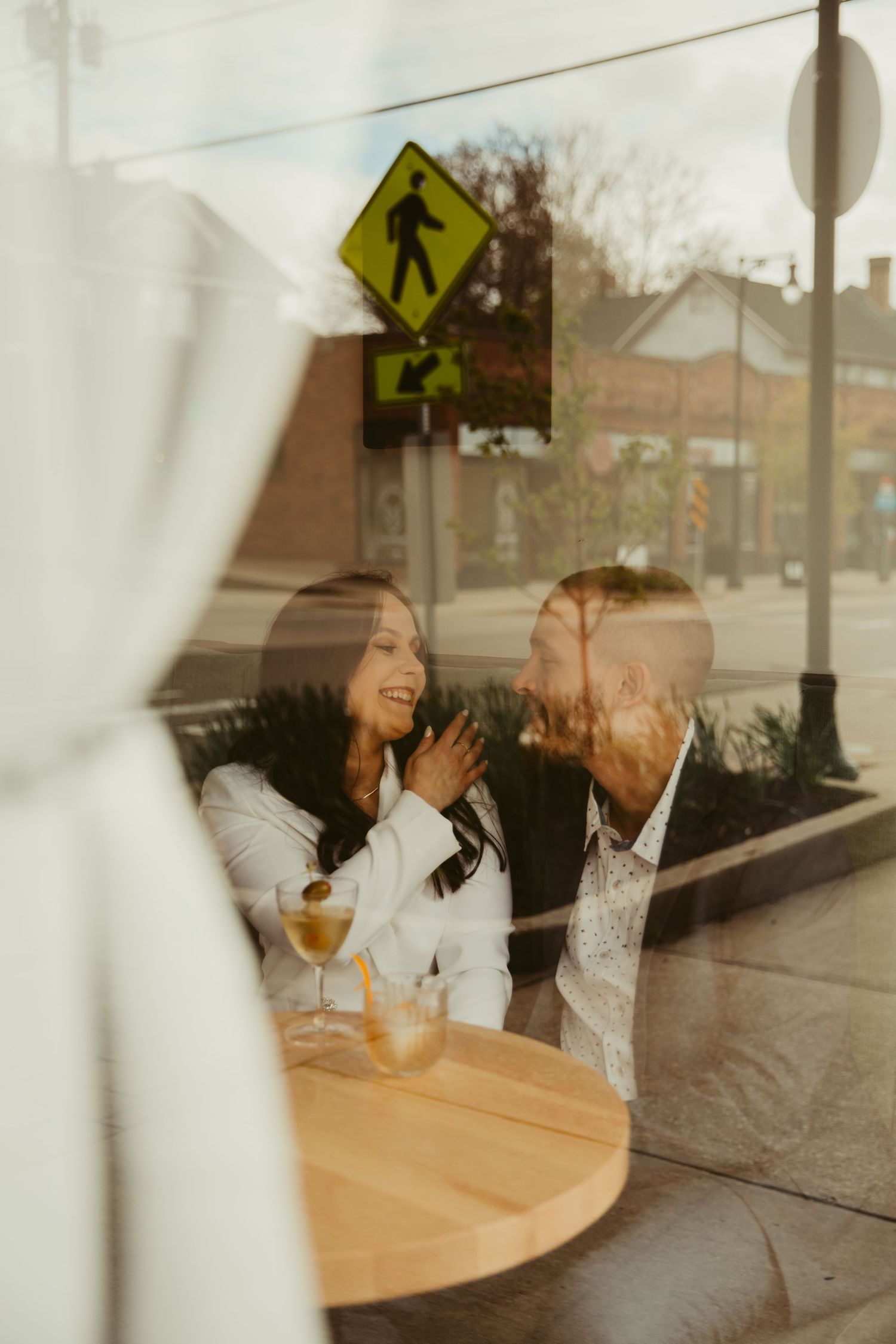 Two people laugh together at a wooden table inside a cafe.